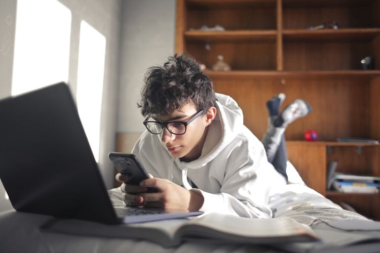 boy studies lying on the bed using computer and smartphone